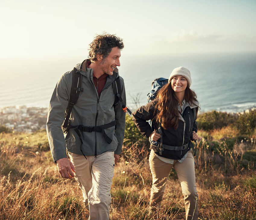 Smiling couple hiking along a coastal trail, using medical cannabis to manage chronic pain and stay active outdoors.
